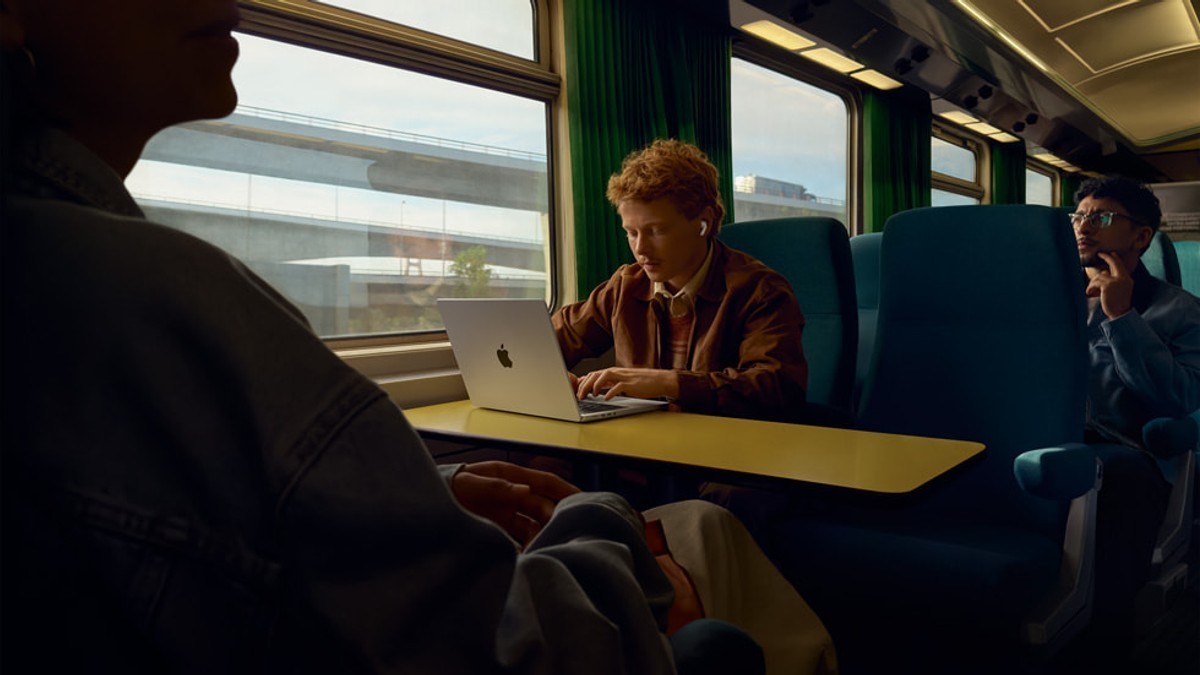 A commuter wearing AirPods Pro 3 while working on a laptop aboard a train.